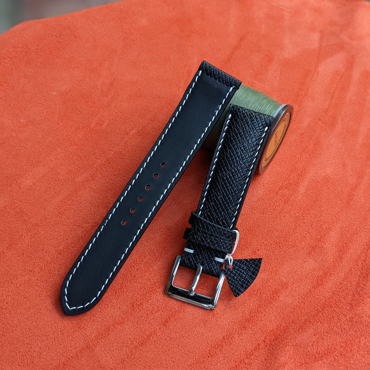 Black watch strap with silver buckle on an orange surface