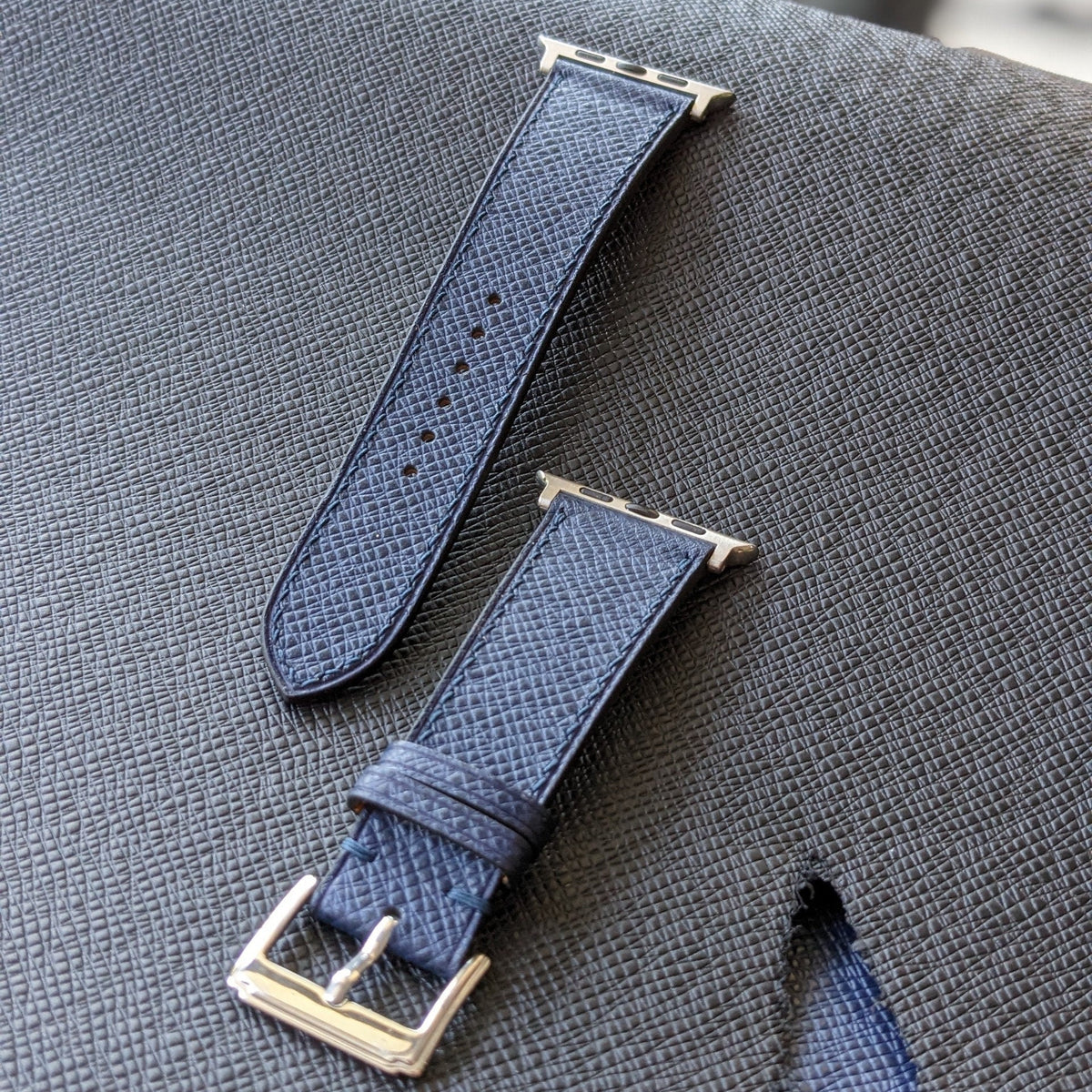Two blue watch straps with silver buckles on a textured gray surface.