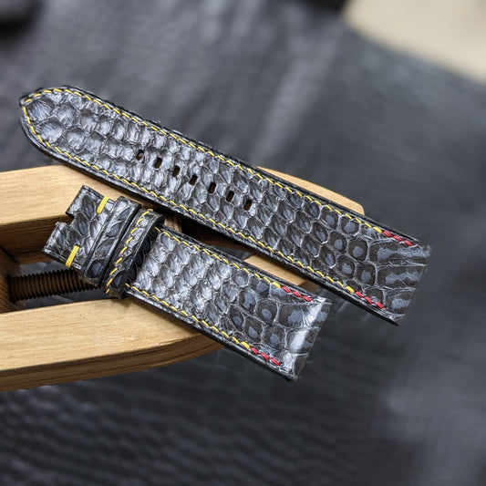 Gray alligator leather watch strap on a wooden stand with a dark textured background